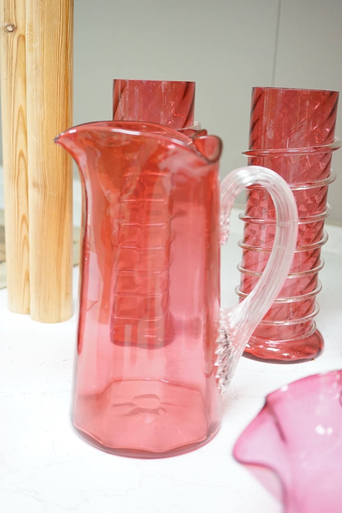 A quantity of cranberry glassware to include pair of vases with trailed decoration, jugs and an oil lamp, largest 38cm high. Condition - fair, some chipping